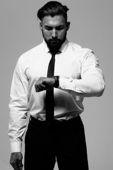 Bearded Hispanic guy in dark vest and white shirt with tie looking at camera with hands in pockets in studio