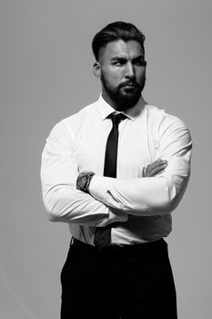 Bearded Hispanic guy in dark vest and white shirt with tie looking at camera with hands in pockets in studio