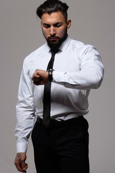 Bearded Hispanic guy in dark vest and white shirt with tie looking at camera with hands in pockets in studio