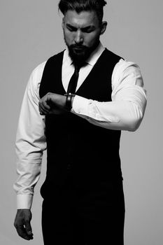 Bearded Hispanic guy in dark vest and white shirt with tie looking at camera with hands in pockets in studio