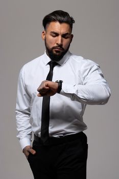 Bearded Hispanic guy in dark vest and white shirt with tie looking at camera with hands in pockets in studio