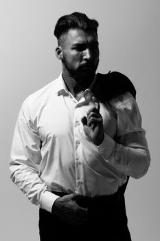 Bearded Hispanic guy in dark vest and white shirt with tie looking at camera with hands in pockets in studio