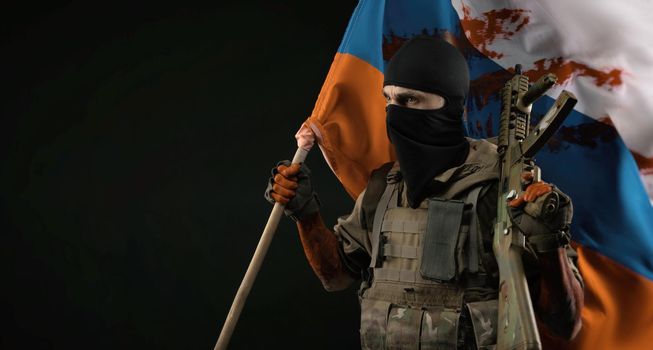 male soldier in a military uniform with a balaclava and hands covered in blood holds a bloody flag of Russia on a black background