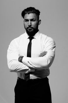 Bearded Hispanic guy in dark vest and white shirt with tie looking at camera with hands in pockets in studio