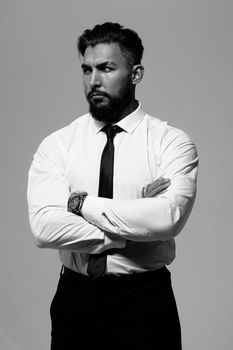 Bearded Hispanic guy in dark vest and white shirt with tie looking at camera with hands in pockets in studio