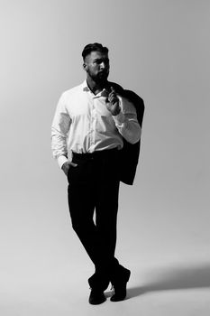 Bearded Hispanic guy in dark vest and white shirt with tie looking at camera with hands in pockets in studio