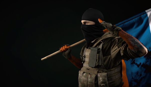 male soldier in a military uniform with a balaclava and hands covered in blood holds a bloody flag of Russia on a black background