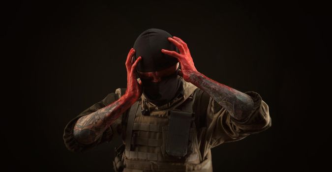 the photo of a man in a military uniform and balaclava with a bloody face and hands up to the elbow in blood on a black background