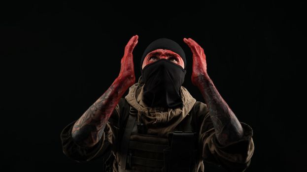 the photo of a man in a military uniform and balaclava with a bloody face and hands up to the elbow in blood on a black background