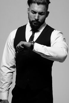 Bearded Hispanic guy in dark vest and white shirt with tie looking at camera with hands in pockets in studio