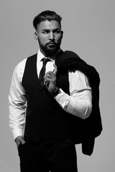 Bearded Hispanic guy in dark vest and white shirt with tie looking at camera with hands in pockets in studio