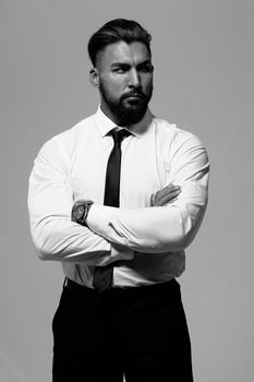 Bearded Hispanic guy in dark vest and white shirt with tie looking at camera with hands in pockets in studio