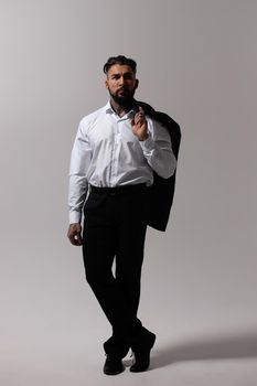 Bearded Hispanic guy in dark vest and white shirt with tie looking at camera with hands in pockets in studio