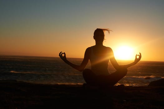 Silhouette of a woman doing a yoga pose against a setting sun.