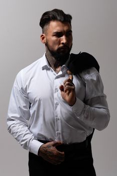 Bearded Hispanic guy in dark vest and white shirt with tie looking at camera with hands in pockets in studio