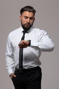 Bearded Hispanic guy in dark vest and white shirt with tie looking at camera with hands in pockets in studio