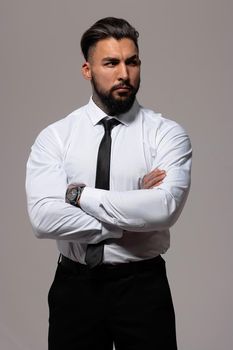 Bearded Hispanic guy in dark vest and white shirt with tie looking at camera with hands in pockets in studio