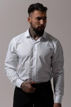 Bearded Hispanic guy in dark vest and white shirt with tie looking at camera with hands in pockets in studio