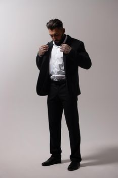 Bearded Hispanic guy in dark vest and white shirt with tie looking at camera with hands in pockets in studio