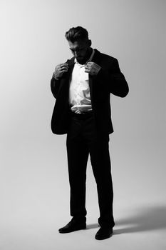 Bearded Hispanic guy in dark vest and white shirt with tie looking at camera with hands in pockets in studio