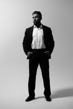 Bearded Hispanic guy in dark vest and white shirt with tie looking at camera with hands in pockets in studio