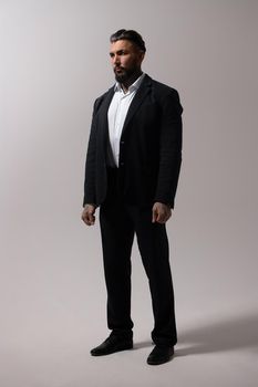 Bearded Hispanic guy in dark vest and white shirt with tie looking at camera with hands in pockets in studio