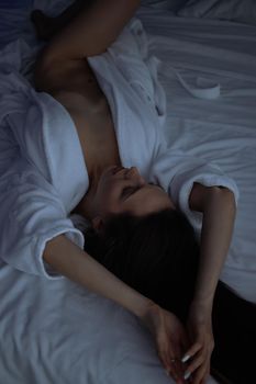 From above of topless sexy female in bathrobe lying on comfortable bed in bedroom
