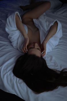 From above of topless sexy female in bathrobe lying on comfortable bed in bedroom