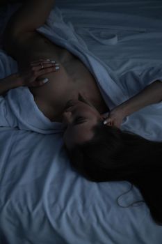 From above of topless sexy female in bathrobe lying on comfortable bed in bedroom