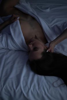 From above of topless sexy female in bathrobe lying on comfortable bed in bedroom
