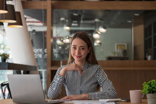 Portrait of charming asian businesswoman sitting working on laptop in office. looking on camera.