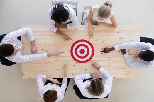 Team of business people pointing at red target at meeting table