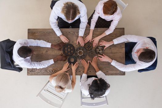 Group of business people joining together metal gears on table at workplace top view