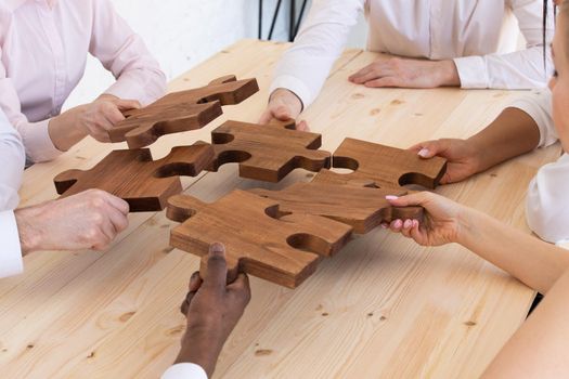 Diverse business people helping in assembling puzzle, cooperation in decision making, team support in solving problems and corporate group teamwork concept, connecting pieces