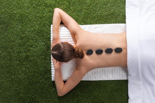 Stone treatment. Top view of beautiful young woman lying on front with spa stones on her back. Beauty treatment concept.