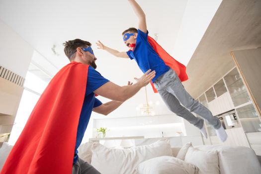 father holding son in superhero costume flying at home