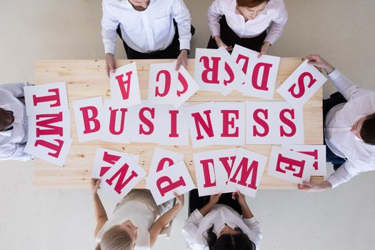 Businesspeople group in business clothes merge letters on paper into word BUSINESS, cooperation unity startup concept