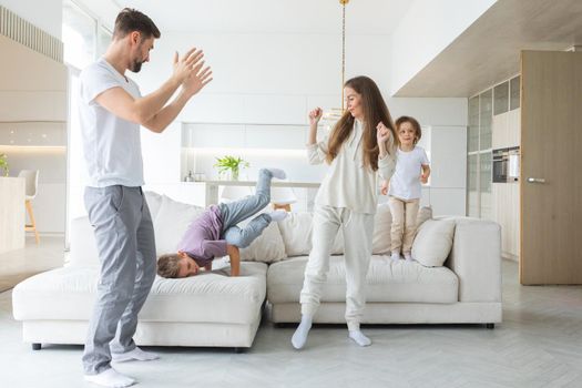 Funny active family of four young adult parents and cute small children dancing together in living room interior, carefree little kids with mum dad having fun laughing enjoy leisure at home