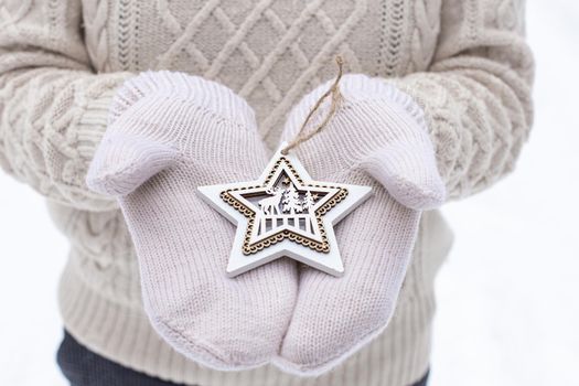 A girl in white mittens and a sweater holds a carved wooden star in her hands. Close up