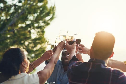 Shot of a group of friends raising up their glasses for a toast while sitting around a table together outdoors.
