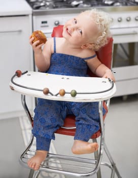 A sweet little baby eating a muffin while sitting in her high chair.