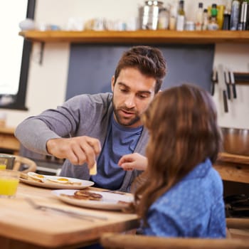 Shot of a little girl eating breakfast with her dad in the kitchen.