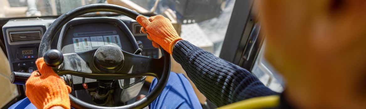 Close up of man in work gloves sitting in vehicle driver cabin and placing hands on steering wheel