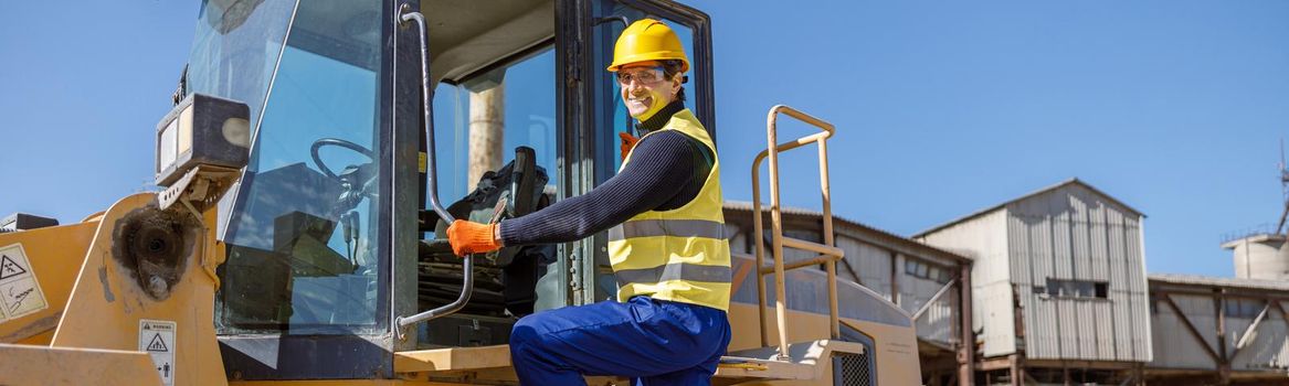 Joyful man factory worker looking at camera and smiling while standing on steps of industrial truck