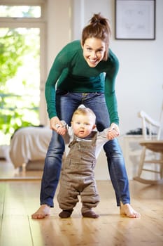 Smiling young mom helping her baby boy learn to walk.