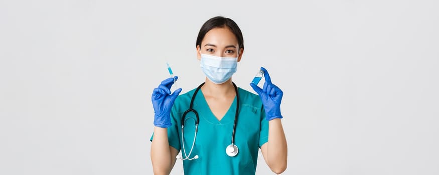 Covid-19, coronavirus disease, healthcare workers concept. Close-up of cute smiling asian female nurse, doctor showing vaccine ampule and syringe, prepare to make injection, white background.