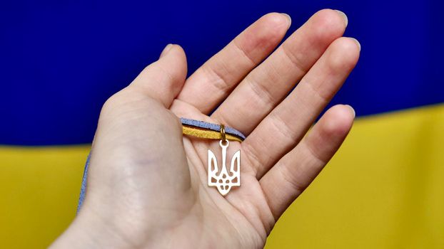 Ukrainian state emblem Trident in the female hand of a Ukrainian woman against the background of a yellow blue flag. War in Ukraine