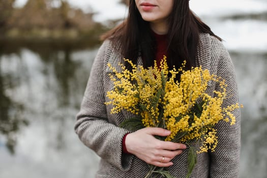 Woman holding bouquet of spring mimosa flowers on nature background.