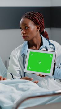Physician holding digital tablet with horizontal green screen, showing technology to patient. Medic and person looking at isolated mockup template and background on chroma key display
