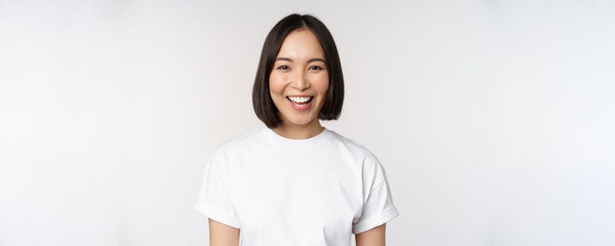 Close up portrait of young asian woman looking at camera, wearing t-shirt, smiling and looking happy, white background.